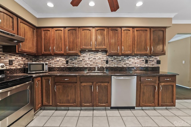 kitchen with sink, light tile patterned floors, appliances with stainless steel finishes, dark stone countertops, and ornamental molding