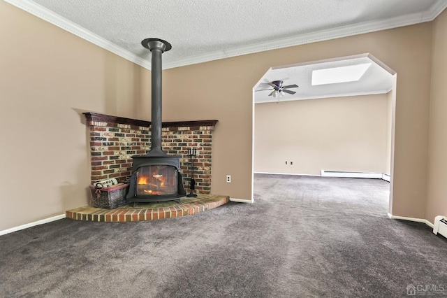 unfurnished living room with ceiling fan, baseboard heating, dark colored carpet, a textured ceiling, and a wood stove