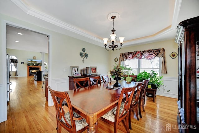 2 Eddie Ct, South Brunswick, NJ 08810 - dining space featuring a raised ceiling, light wood-style flooring, wainscoting, a chandelier, and a warm lit fireplace