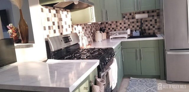 kitchen with light countertops, backsplash, appliances with stainless steel finishes, wall chimney range hood, and green cabinetry