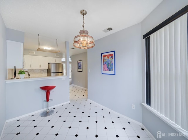 kitchen with baseboards, visible vents, freestanding refrigerator, light countertops, and backsplash