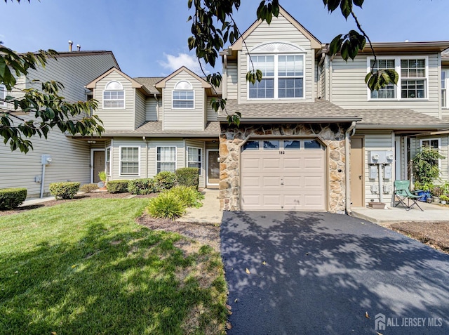 townhome / multi-family property with aphalt driveway, stone siding, a shingled roof, a front yard, and an attached garage