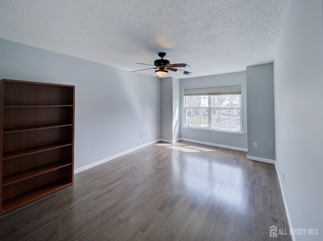 spare room featuring baseboards, dark wood-type flooring, ceiling fan, and a textured ceiling