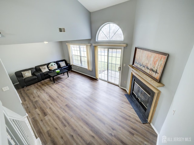 unfurnished living room featuring visible vents, baseboards, a fireplace with flush hearth, a high ceiling, and wood finished floors