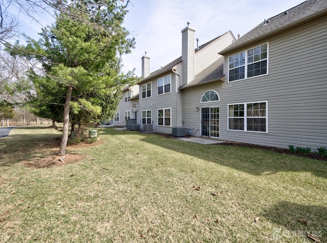 back of house with central AC unit, a lawn, and a chimney