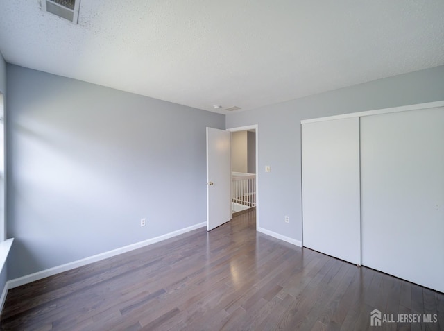 unfurnished bedroom featuring wood finished floors, visible vents, baseboards, a closet, and a textured ceiling