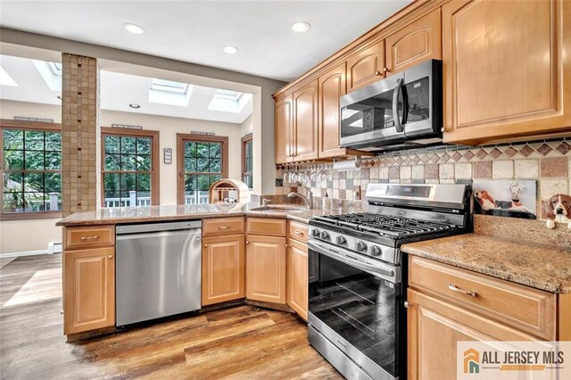 5 Serviss Ave, East Brunswick, NJ 08816 - kitchen with appliances with stainless steel finishes, a skylight, light brown cabinetry, a peninsula, and light wood-type flooring