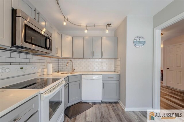 kitchen with gray cabinets, backsplash, a sink, light wood-type flooring, and white appliances