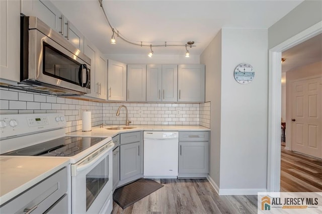 kitchen featuring a sink, light wood finished floors, white appliances, light countertops, and gray cabinets