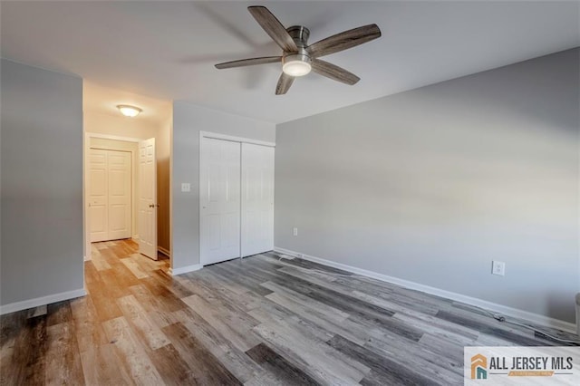 unfurnished bedroom featuring baseboards, ceiling fan, a closet, and wood finished floors