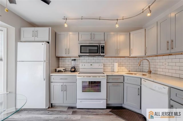 kitchen featuring tasteful backsplash, a sink, gray cabinetry, light wood-style floors, and white appliances