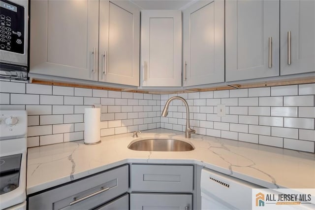 kitchen featuring backsplash, stainless steel microwave, a sink, and gray cabinets