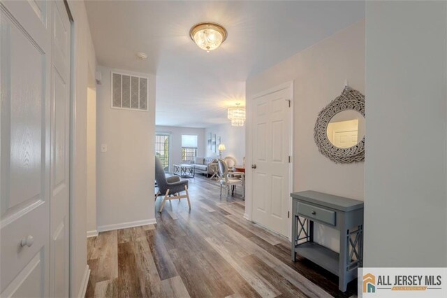 hall featuring baseboards, visible vents, a chandelier, and wood finished floors