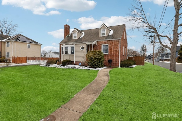 new england style home featuring brick siding, a chimney, a front yard, and fence