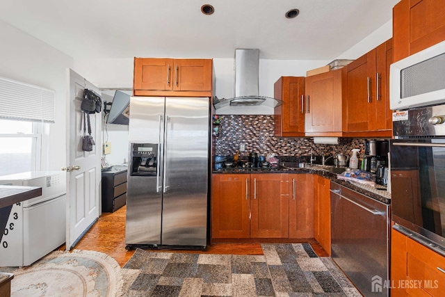 kitchen with tasteful backsplash, brown cabinetry, wall chimney range hood, and black appliances