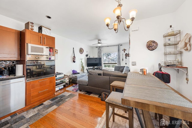 kitchen featuring ceiling fan with notable chandelier, stainless steel appliances, open floor plan, light wood finished floors, and tasteful backsplash