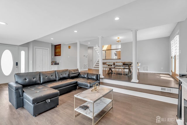 living area featuring stairway, decorative columns, wood finished floors, and visible vents