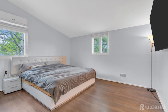 bedroom featuring a wall mounted air conditioner, baseboards, wood finished floors, lofted ceiling, and visible vents