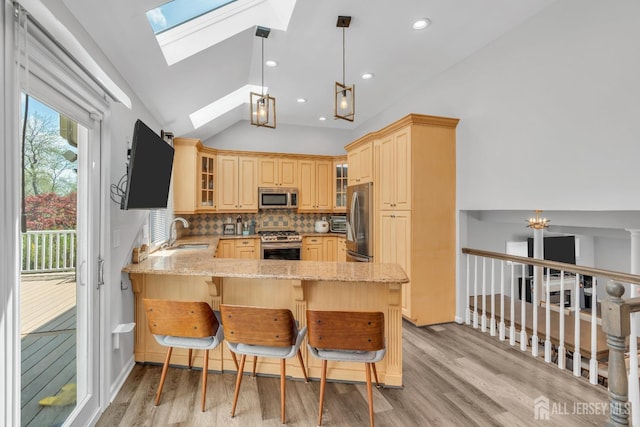 kitchen with light stone countertops, appliances with stainless steel finishes, vaulted ceiling with skylight, light wood-style floors, and a peninsula