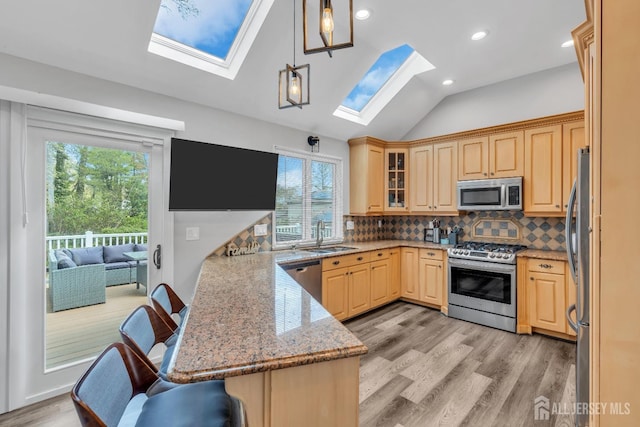 kitchen featuring backsplash, appliances with stainless steel finishes, a sink, a peninsula, and light wood-style flooring