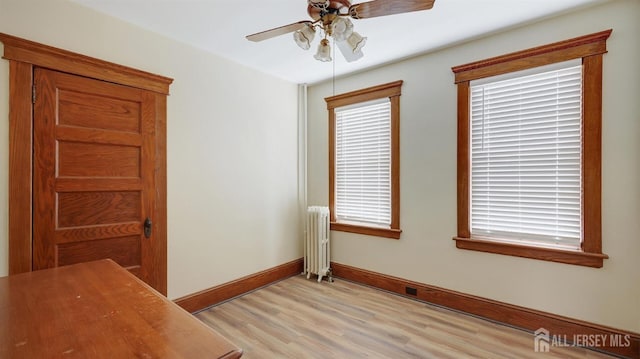 unfurnished room with radiator, baseboards, light wood-type flooring, and ceiling fan