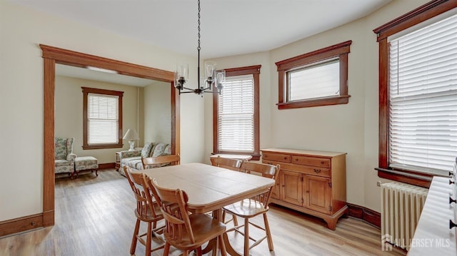 dining room with baseboards, a chandelier, radiator heating unit, and light wood finished floors