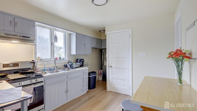 kitchen with a sink, gray cabinets, stainless steel range with gas cooktop, light wood-type flooring, and under cabinet range hood