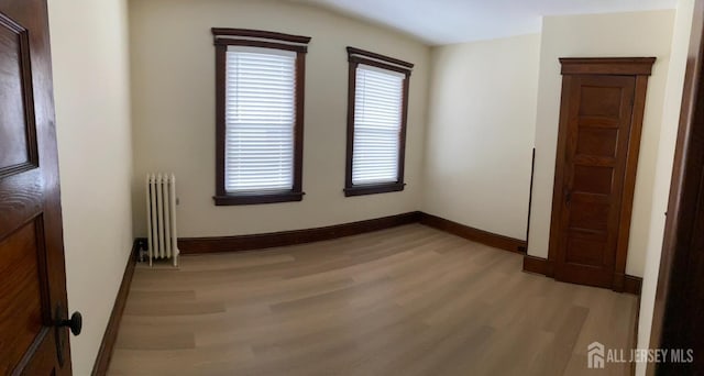 unfurnished room with baseboards, radiator, and light wood-style floors