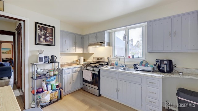 kitchen featuring stainless steel gas range oven, a sink, light countertops, light wood finished floors, and under cabinet range hood