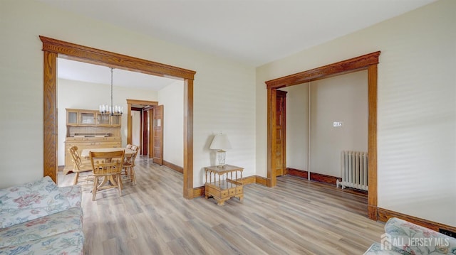 living room with radiator, baseboards, light wood finished floors, and a notable chandelier