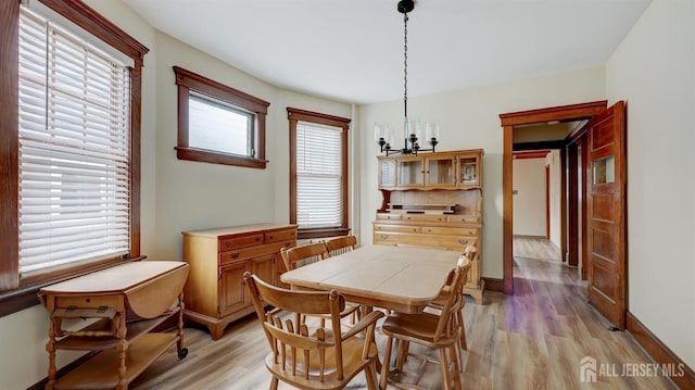 dining area featuring light wood-type flooring, baseboards, and a notable chandelier