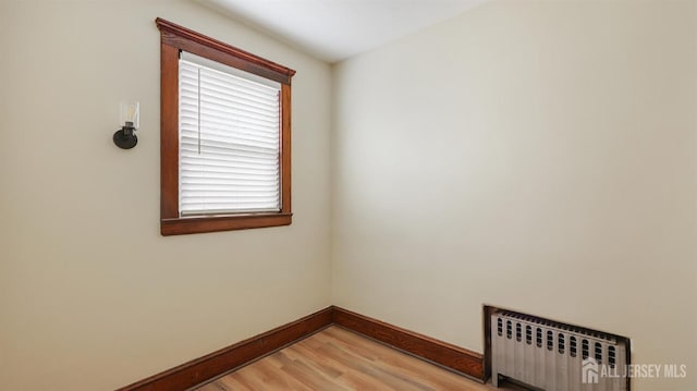empty room with baseboards, light wood finished floors, and radiator heating unit