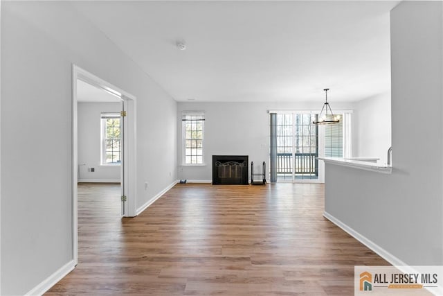 unfurnished living room featuring a notable chandelier, baseboards, and wood finished floors