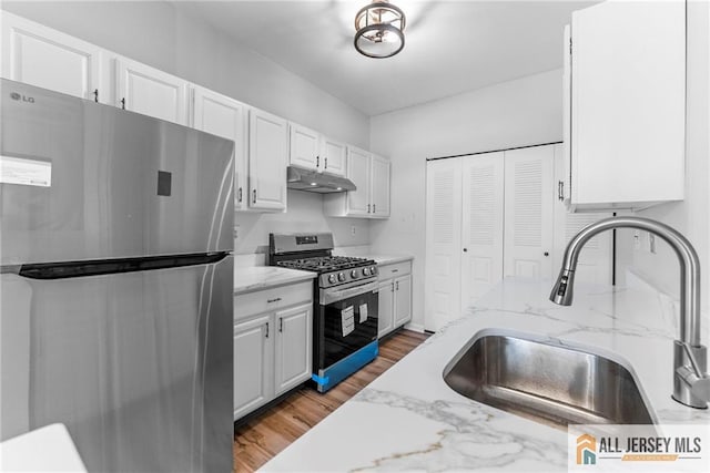 kitchen with light wood-style flooring, under cabinet range hood, a sink, stainless steel appliances, and white cabinets