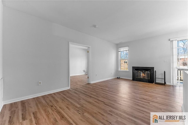 unfurnished living room with a fireplace with flush hearth, wood finished floors, and baseboards