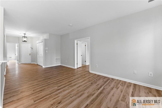 unfurnished living room featuring visible vents, baseboards, and wood finished floors