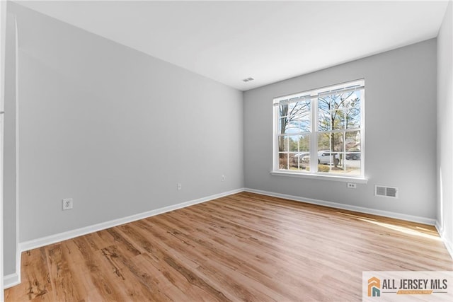 empty room featuring light wood finished floors, visible vents, and baseboards