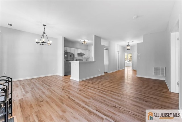 unfurnished living room with baseboards, light wood-style floors, visible vents, and a chandelier