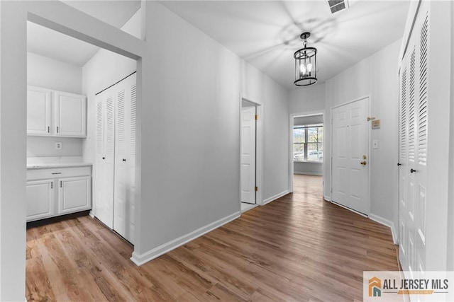 hallway featuring visible vents, light wood-style flooring, an inviting chandelier, and baseboards