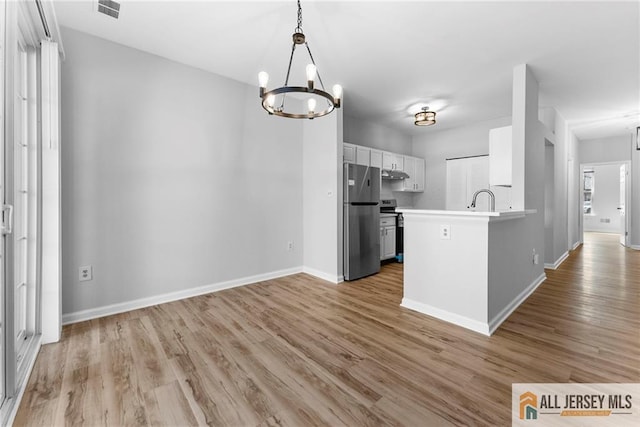 kitchen featuring light wood finished floors, baseboards, stainless steel appliances, a notable chandelier, and white cabinetry