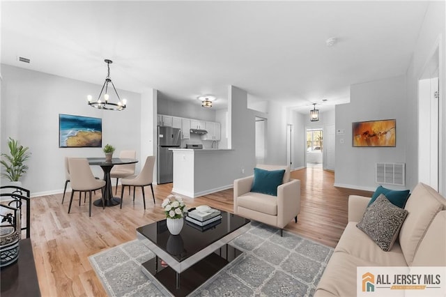 living room with an inviting chandelier, light wood-style flooring, baseboards, and visible vents