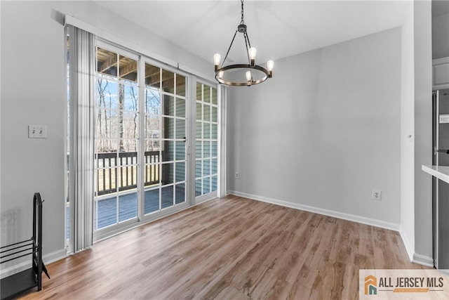 unfurnished dining area featuring wood finished floors, baseboards, and a chandelier