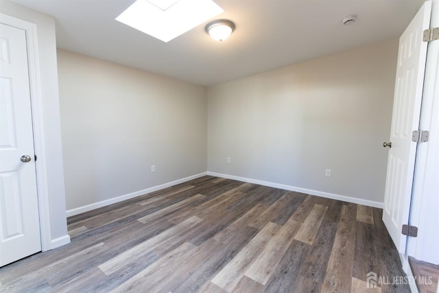 empty room with dark wood-type flooring and a skylight