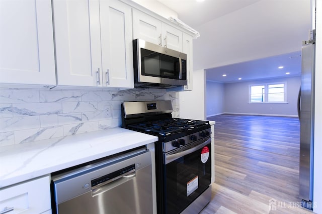 kitchen featuring stainless steel appliances, white cabinetry, light wood-type flooring, light stone countertops, and tasteful backsplash