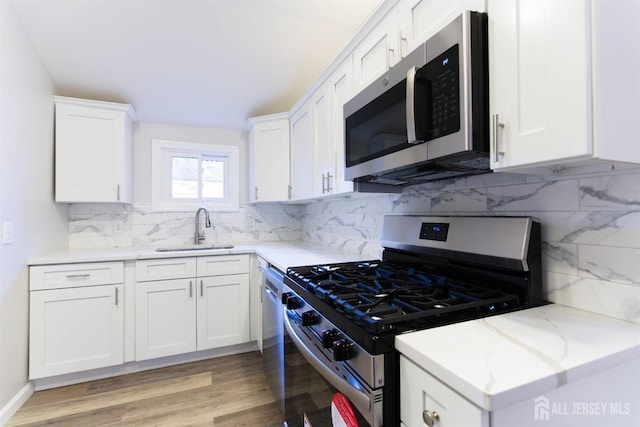 kitchen featuring light wood finished floors, decorative backsplash, appliances with stainless steel finishes, white cabinetry, and a sink