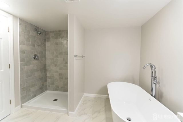 bathroom with marble finish floor, tiled shower, a freestanding bath, and baseboards