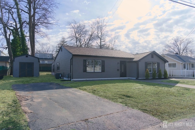 ranch-style house featuring aphalt driveway, a storage unit, an outdoor structure, and a front yard