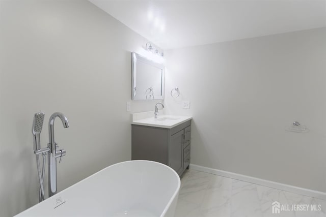 bathroom with marble finish floor, baseboards, a freestanding tub, and vanity