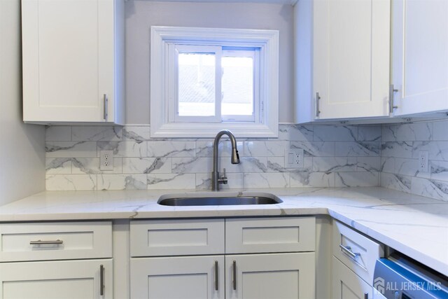 kitchen featuring white cabinets, backsplash, light stone countertops, and sink