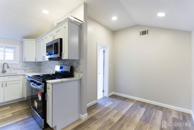 kitchen featuring stainless steel appliances, light countertops, visible vents, vaulted ceiling, and a sink